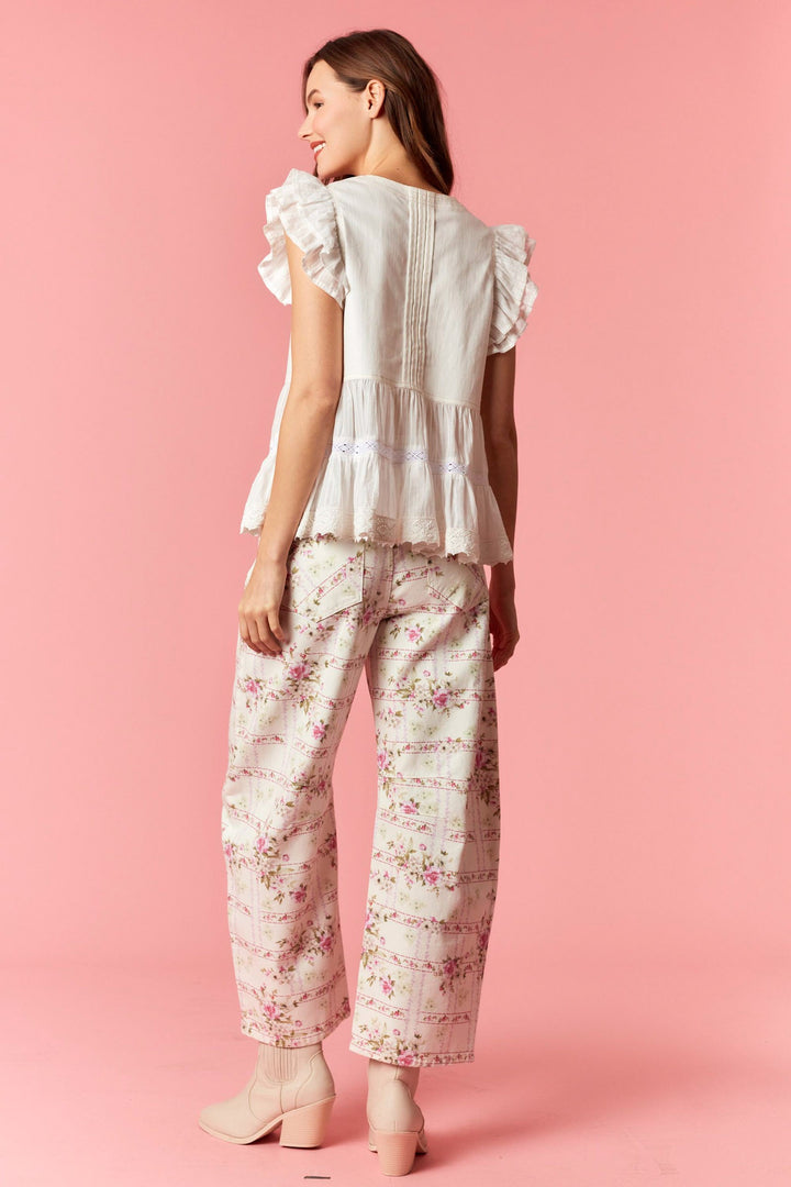 Woman wearing a white blouse with ruffled sleeves and floral pants on a pink background