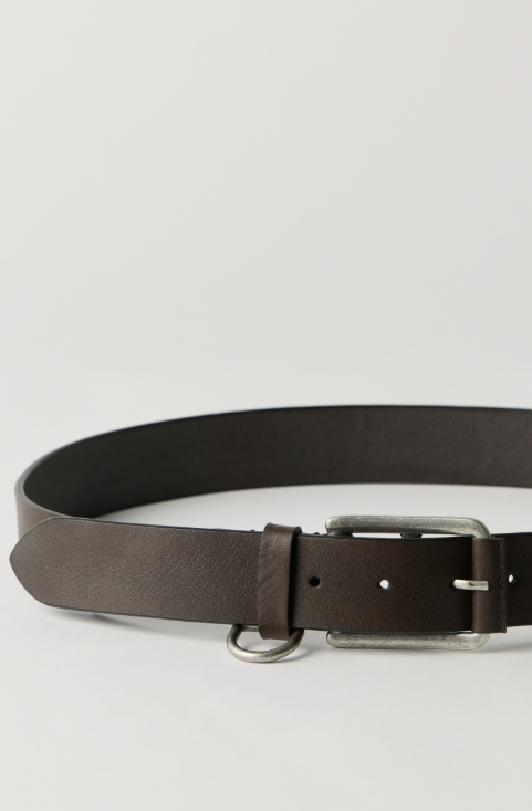 A dark brown leather belt with a silver-toned metal buckle and D-ring, photographed on a light gray studio background.