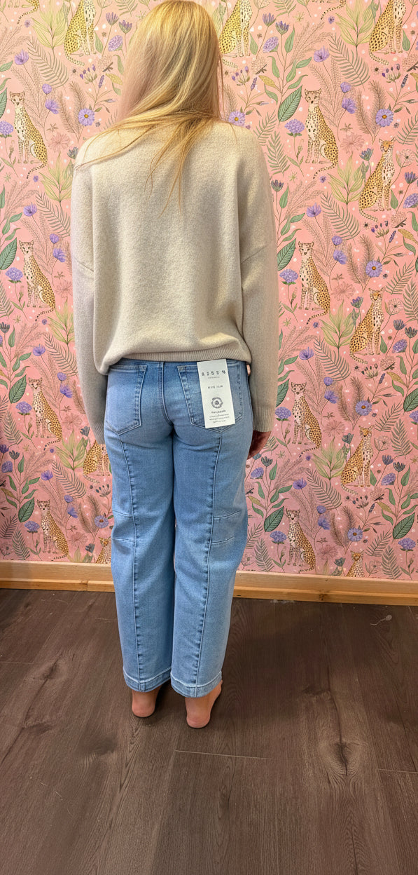 A person standing in a room wearing light blue straight-leg jeans and a beige cardigan, photographed from behind against a pink patterned wallpaper background.
