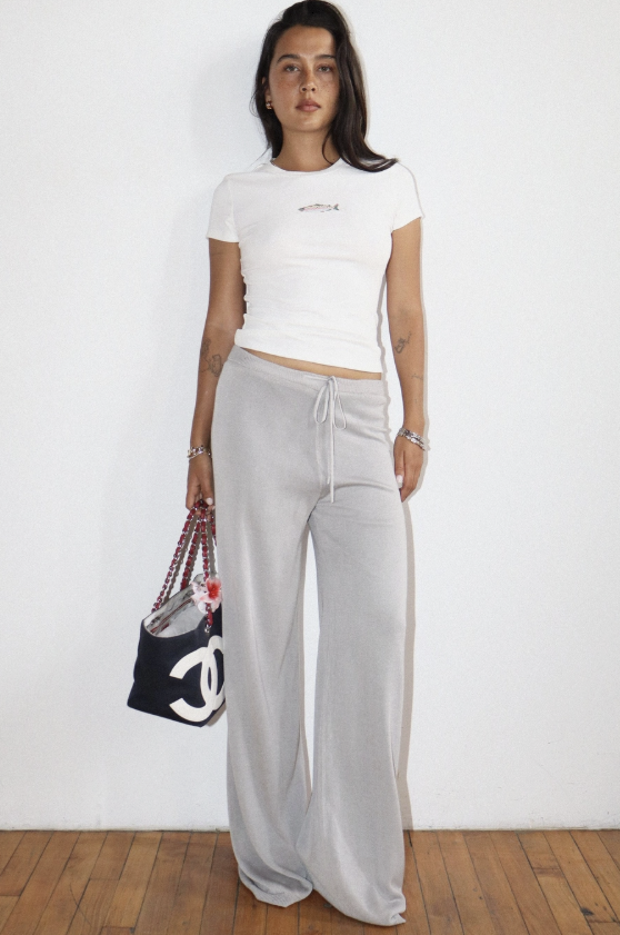 Person wearing a white crop top and gray sweatpants, holding a black handbag with a brand logo.