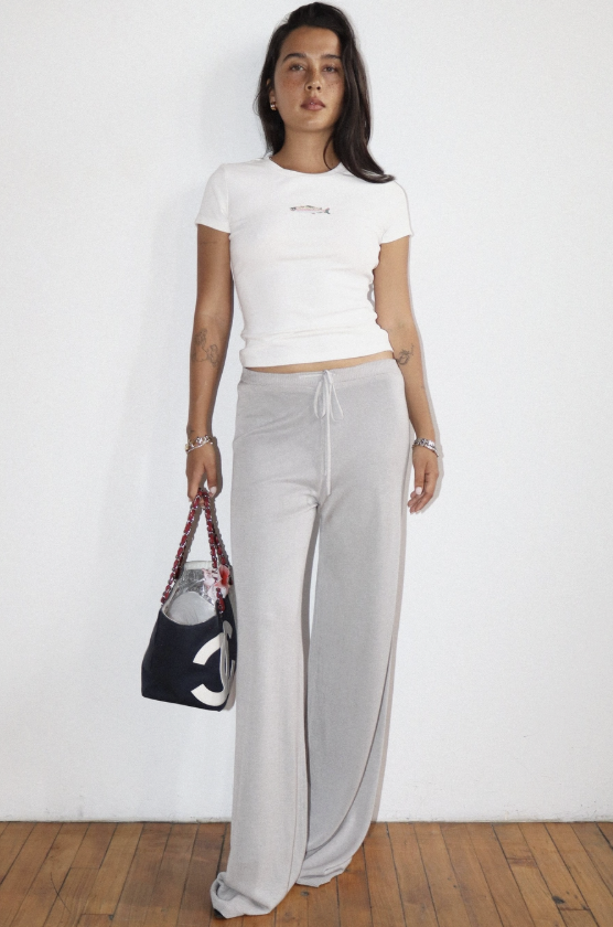 Woman wearing a white t-shirt and gray pants holding a black handbag against a white background
