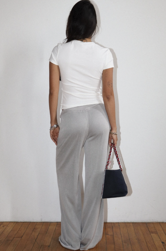 Person wearing a white top and light gray pants against a plain background