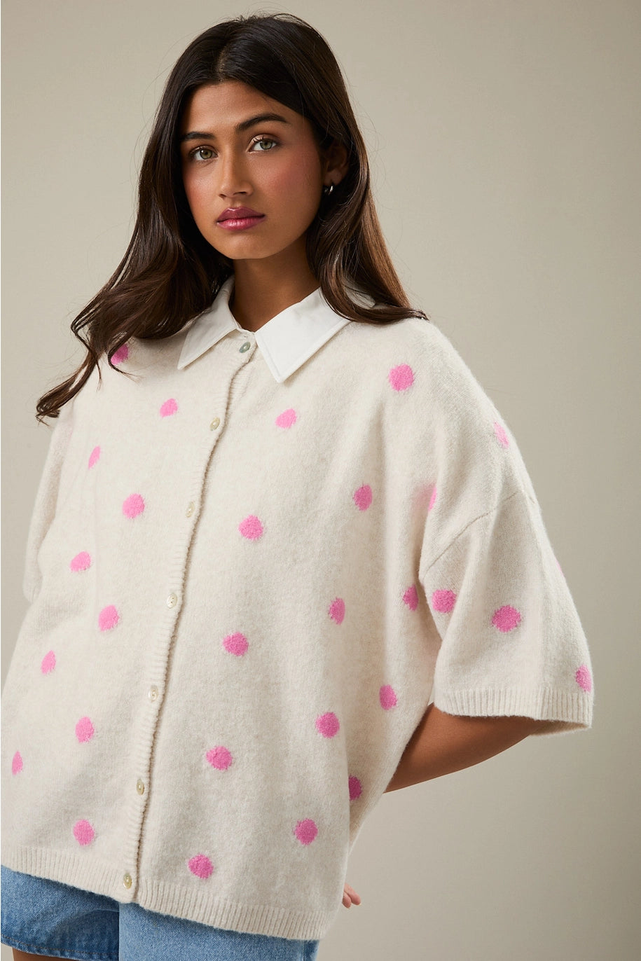Woman wearing a cream-colored poncho with pink polka dots on a neutral background