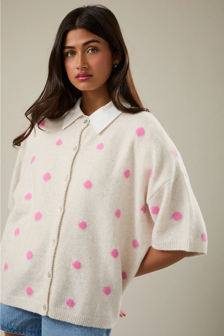 Woman wearing a cream-colored poncho with pink polka dots on a neutral background