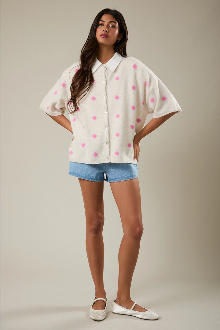 Woman wearing a white blouse with pink polka dots and denim shorts on a beige background