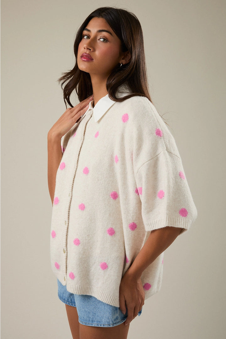 Woman wearing a white poncho with pink polka dots against a neutral background