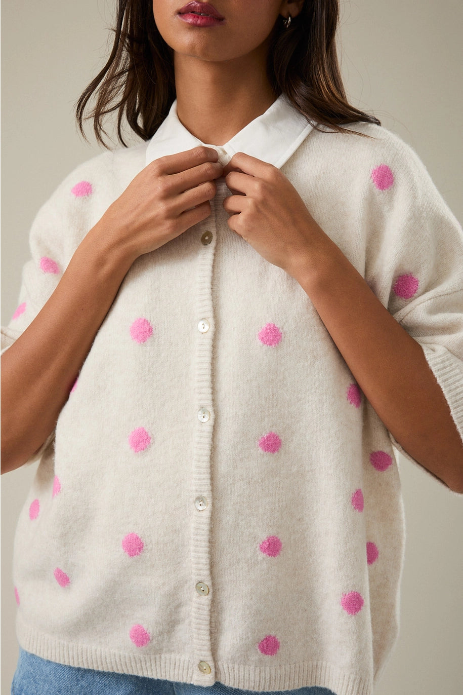 Woman wearing a cream cardigan with pink polka dots on a neutral background