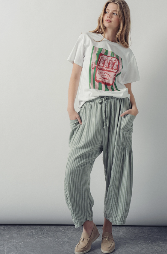 Woman wearing a white t-shirt with a graphic design and green striped pants against a plain background
