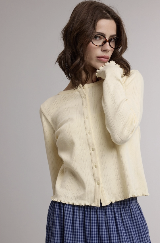 Woman wearing yellow cardigan and blue skirt on plain background