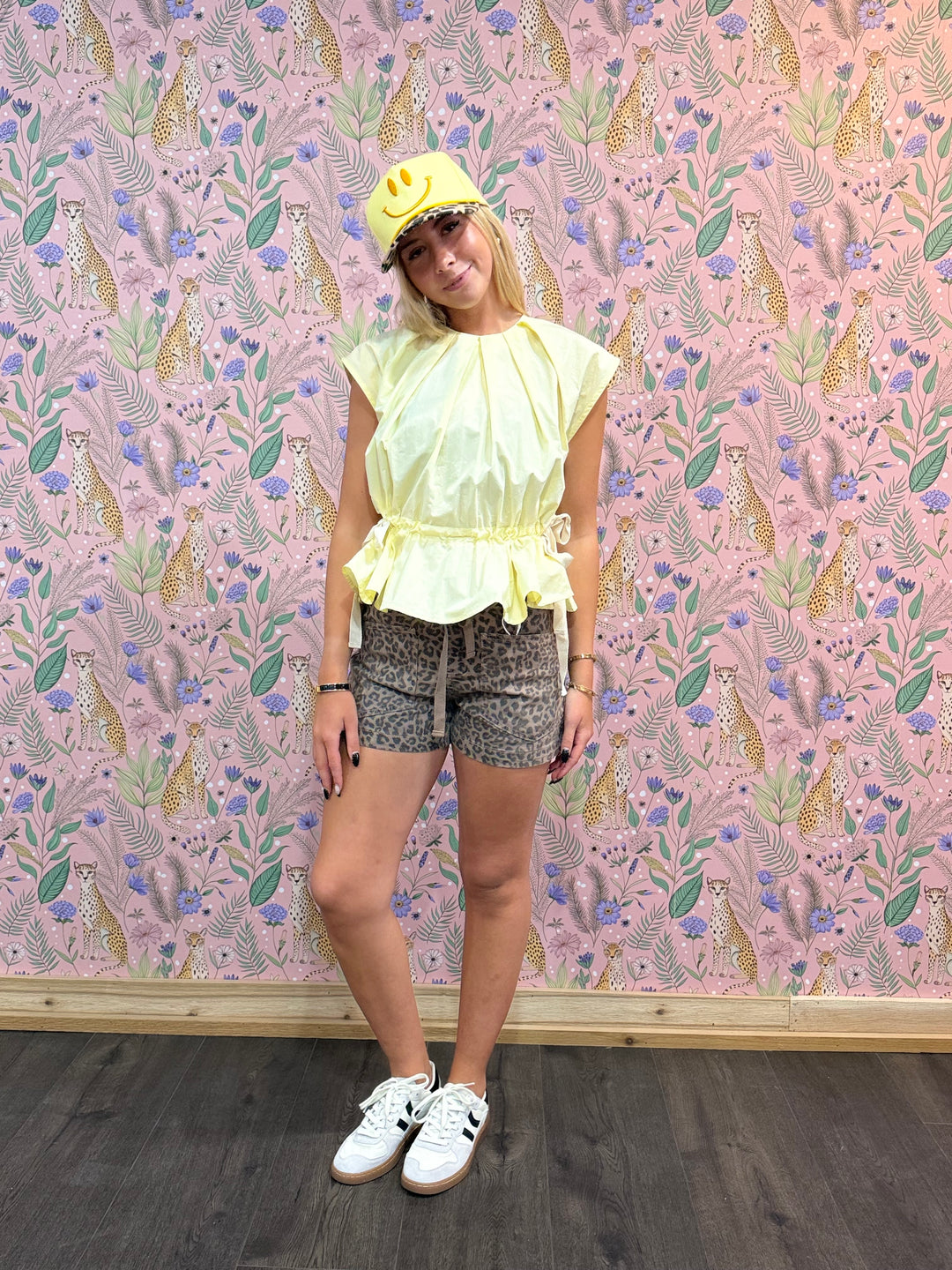 Person wearing a yellow top and shorts standing against a pink floral-patterned wall.