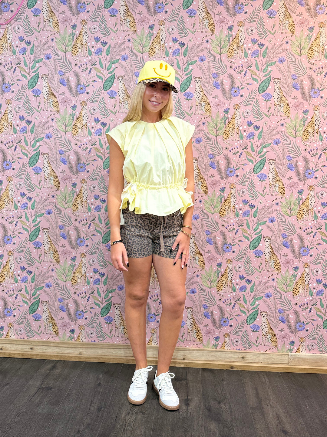 Person wearing a yellow top and patterned shorts standing against a floral wallpapered wall.
