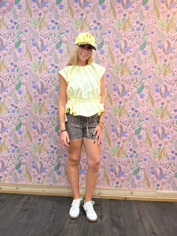 Person wearing a yellow top and patterned shorts standing against a floral wallpapered wall.