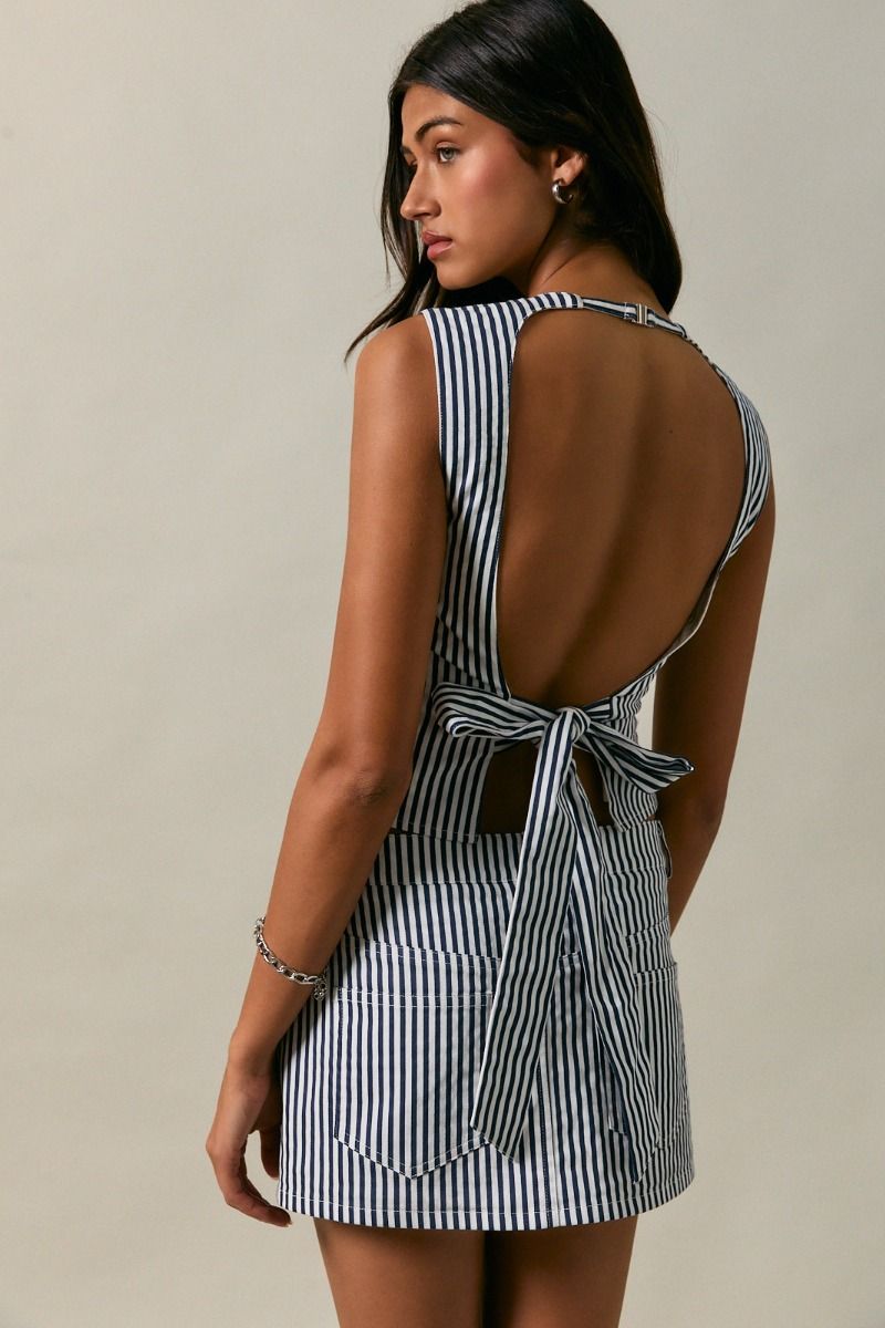 Woman wearing a navy and white striped dress with a tie waist on a beige background