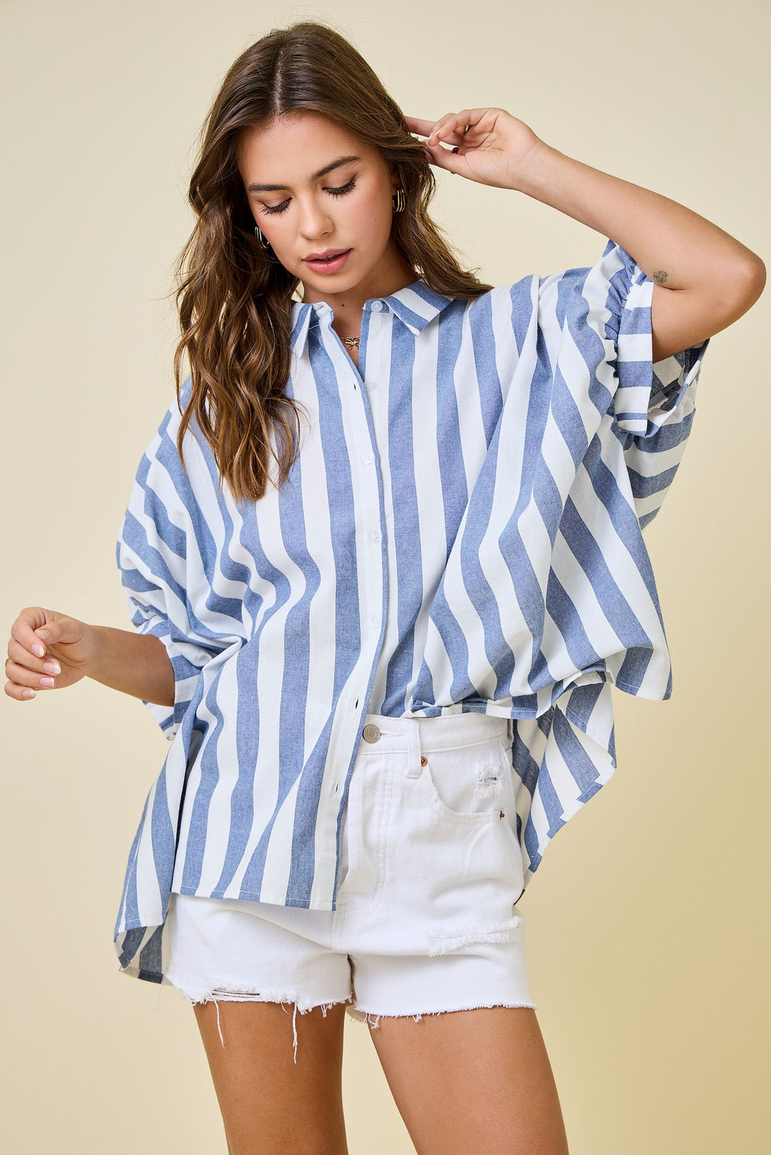 Woman wearing a blue and white striped shirt and white shorts on a beige background
