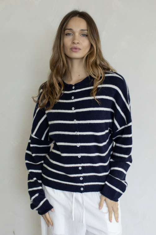 Woman wearing navy and white stripe cardigan and white pants on plain background