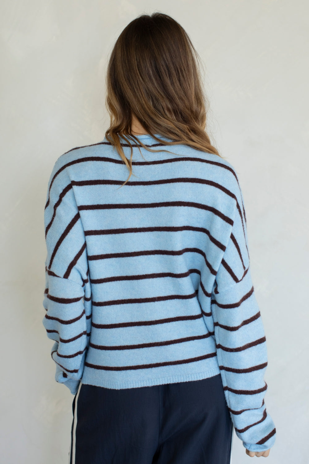 Person wearing a light blue and brown striped sweater against a white background