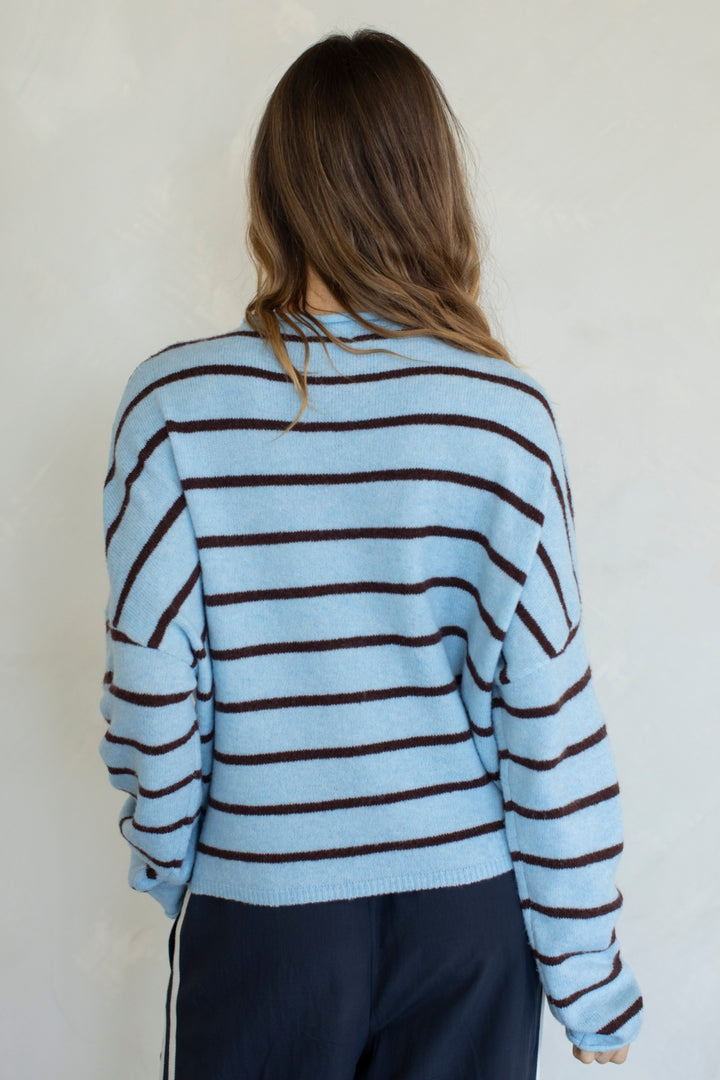 Person wearing a light blue and brown striped sweater against a white background
