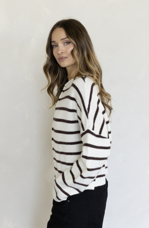 Woman wearing white and brown stripe cardigan and black pants on plain background