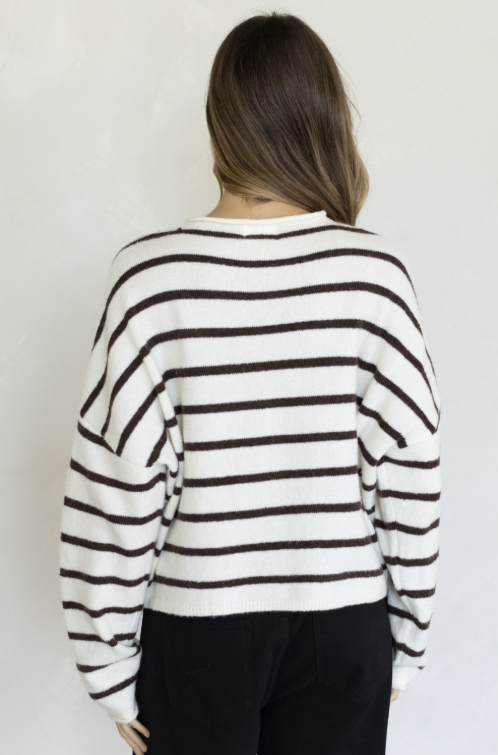Woman shown from behind wearing white and brown cardigan and black pants on plain background