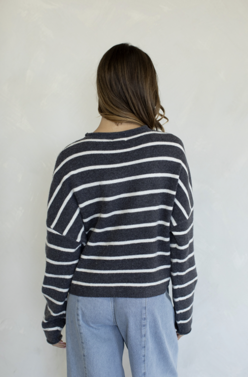 Woman shown from behind wearing grey and white stripe cardigan and jeans on plain background