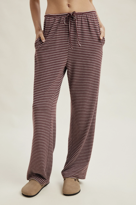 A person wearing loose, wide-leg striped lounge pants with a drawstring waist and side pockets, paired with tan slip-on shoes, photographed against a plain light beige studio background.