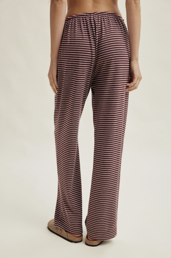 A person shown from the back wearing loose, wide-leg pants with horizontal burgundy and beige stripes, photographed against a plain light studio background.