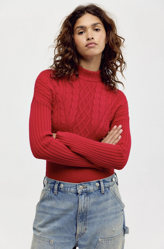 Woman wearing red mock neck bodysuit with light denim jeans on white background