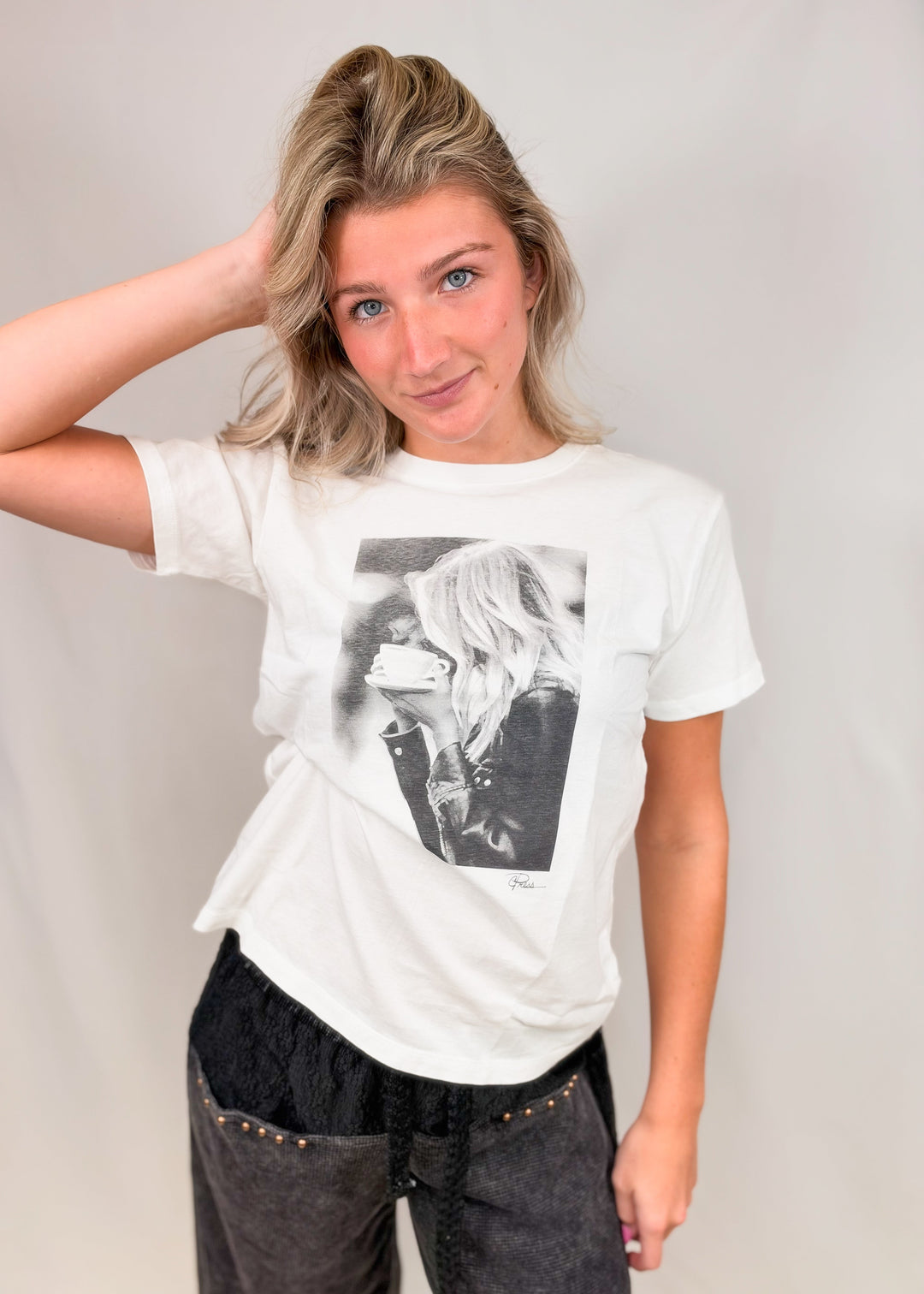 Woman wearing graphic tee with drawing of woman drinking coffee on plain background