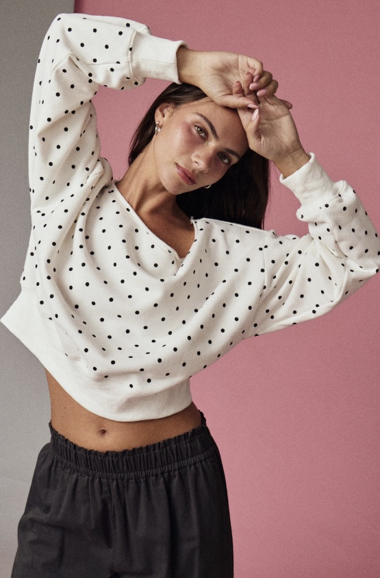 Woman wearing white sweatshirt with black polka dots on pink background