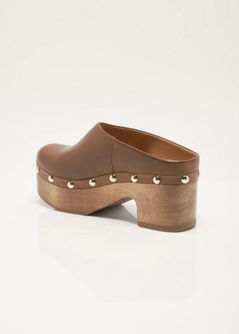 A brown leather clog shoe with a wooden block heel and platform, decorated with small gold-tone metal studs, shown from a side-rear angle on a white background.
