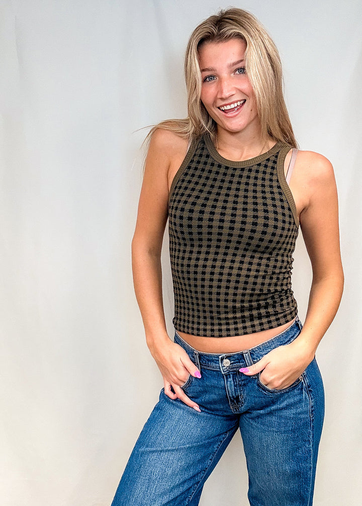 Woman wearing olive green houndstooth tank top with blue jeans on white background