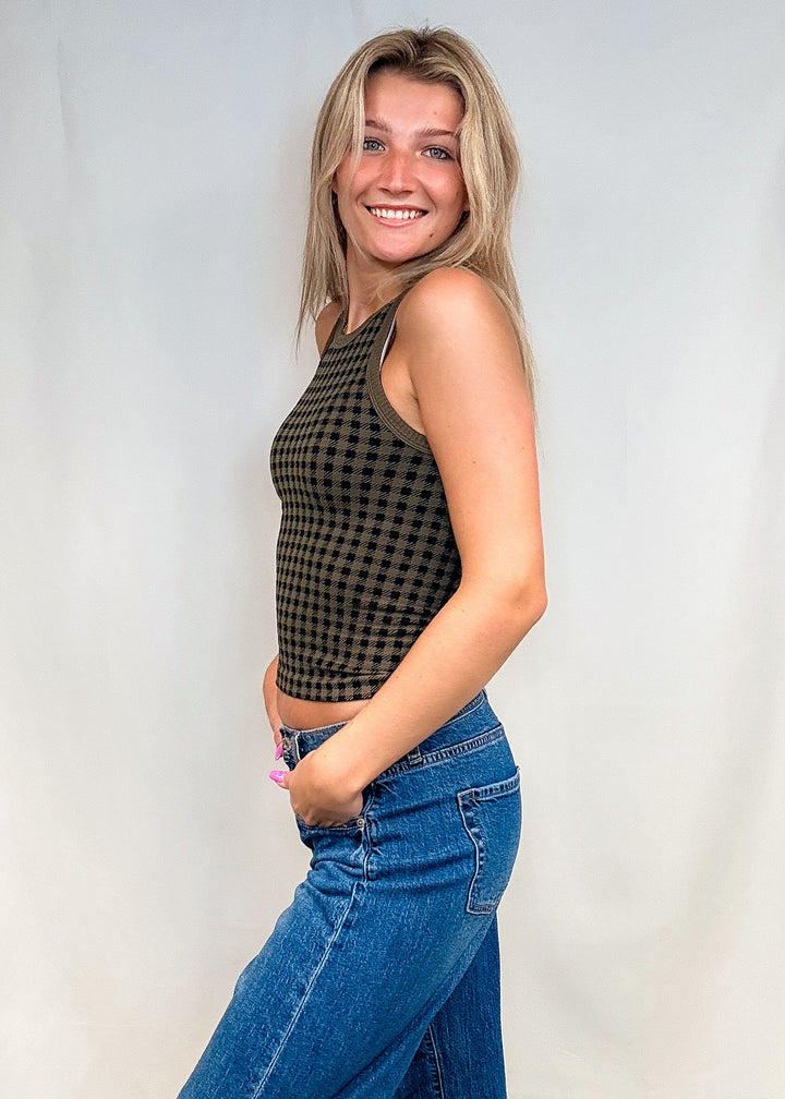 Woman wearing olive green houndstooth tank top with blue jeans on white background