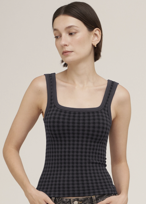 A woman modeling a black and dark gray checkered ribbed tank top with a square neckline, photographed against a solid light beige background.