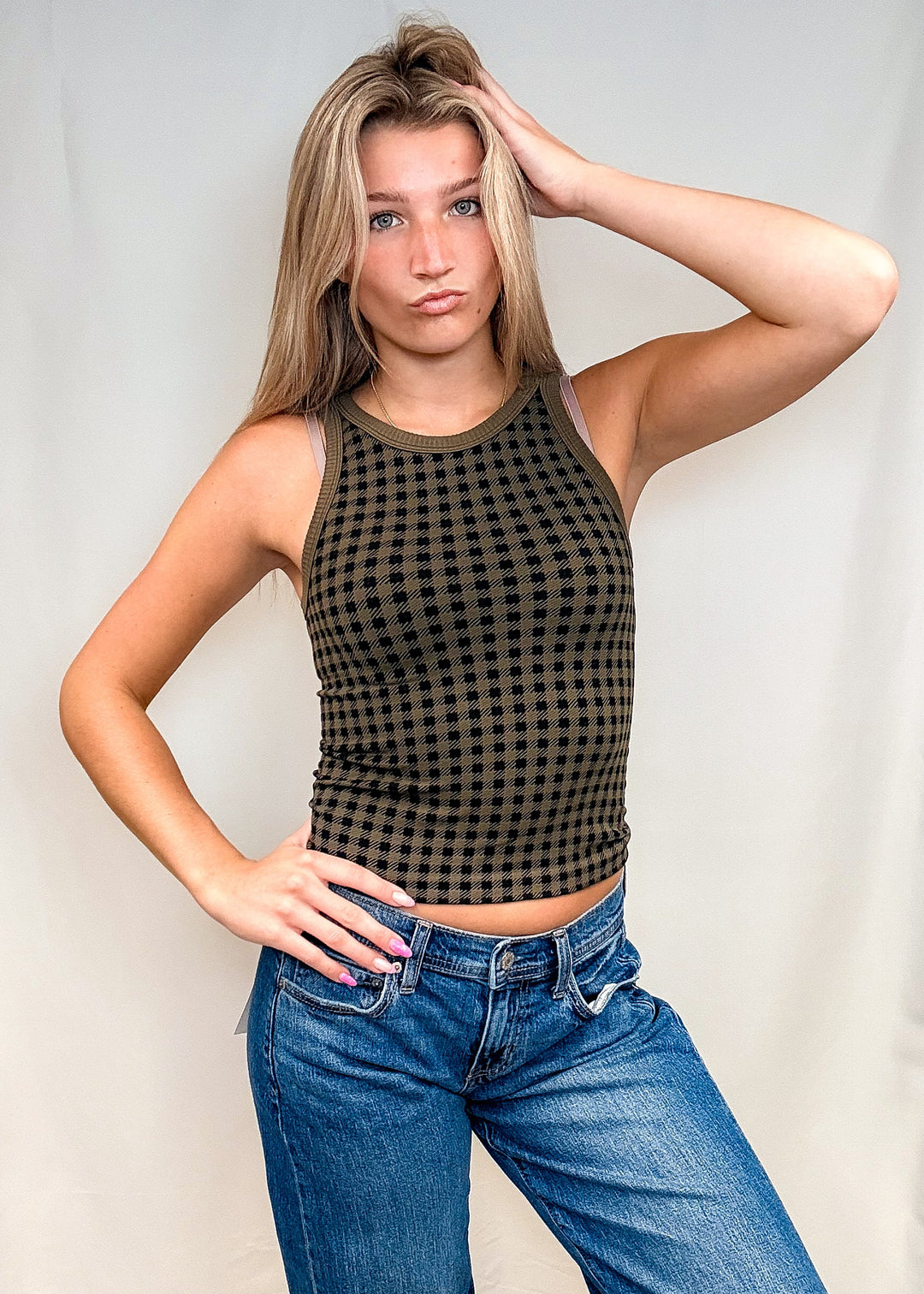 Woman wearing olive green houndstooth tank top with blue jeans on white background