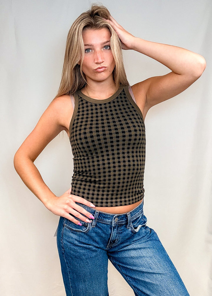 Woman wearing olive green houndstooth tank top with blue jeans on white background