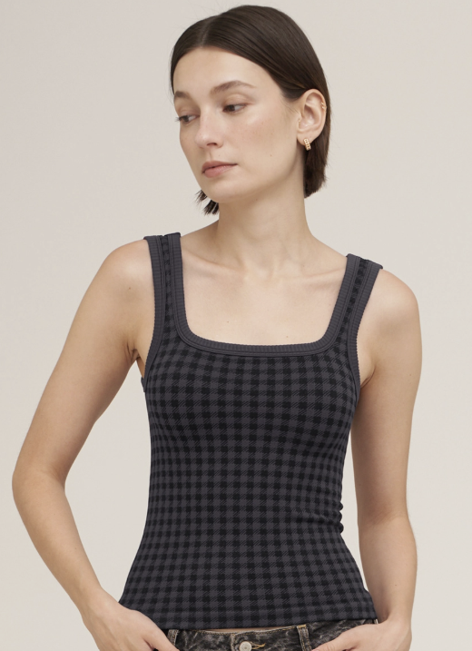 A woman modeling a black and dark gray checkered ribbed tank top with a square neckline, photographed against a solid light beige background.