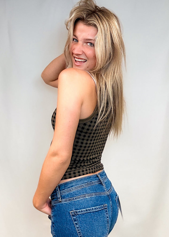 Woman wearing olive green houndstooth tank top with blue jeans on white background