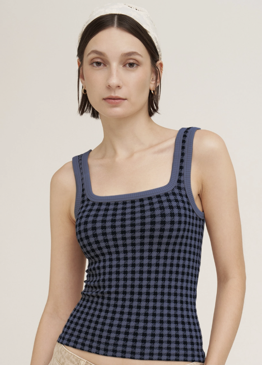 A woman wearing a navy and black gingham patterned ribbed tank top with a square neckline and wide straps, paired with a white headband and beige bottoms, against a solid light beige background.
