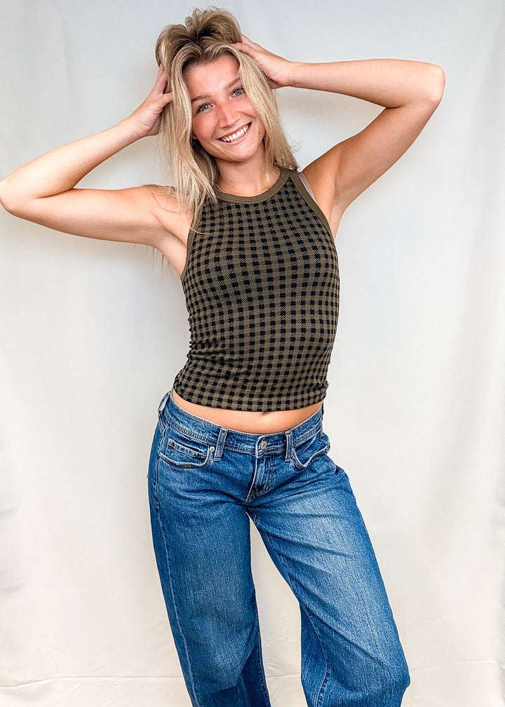Woman wearing olive green houndstooth tank top with blue jeans on white background
