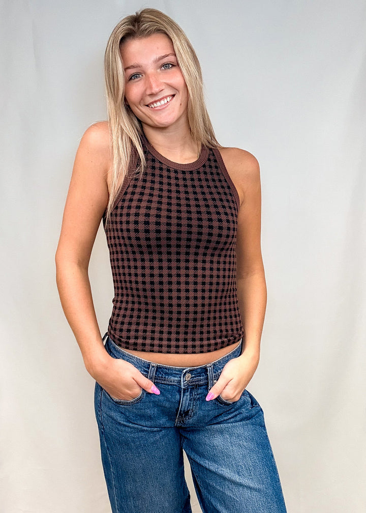 Woman wearing brown houndstooth tank top with blue jeans on white background