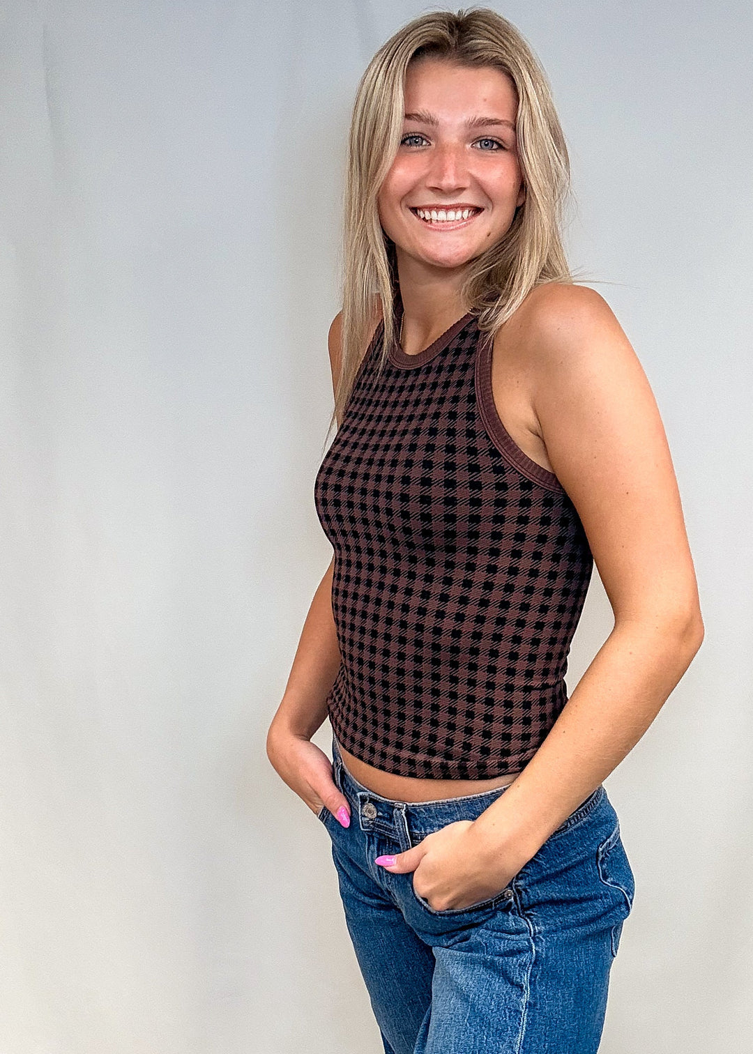 Woman wearing brown houndstooth tank top with blue jeans on white background