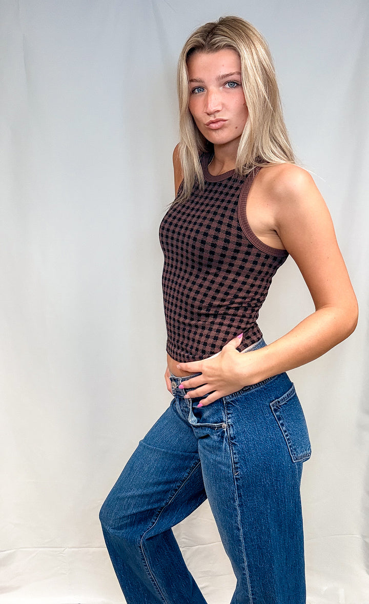 Woman wearing brown houndstooth tank top with blue jeans on white background