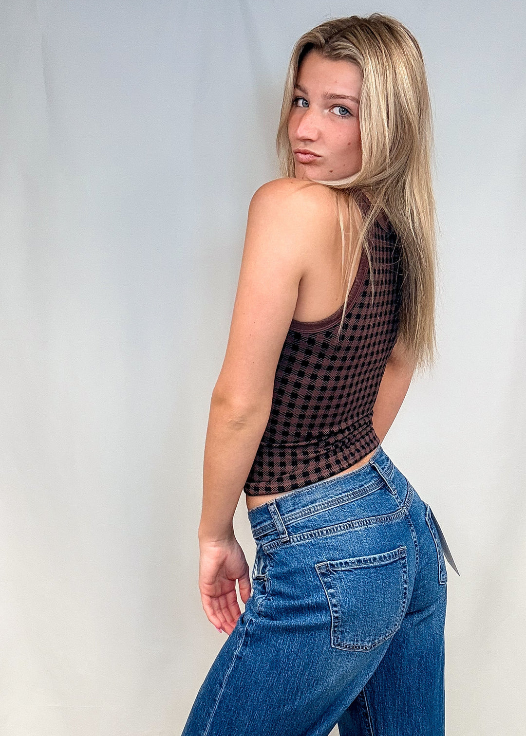 Woman wearing brown houndstooth tank top with blue jeans on white tank top