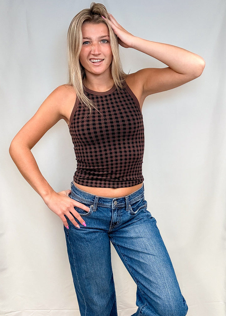 Woman wearing brown houndstooth tank top with blue jeans on white background