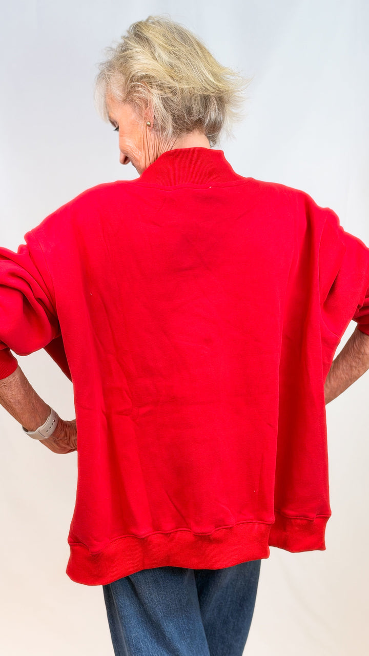 Woman shown from back wearing red mock neck sweatshirt and jeans on plain background