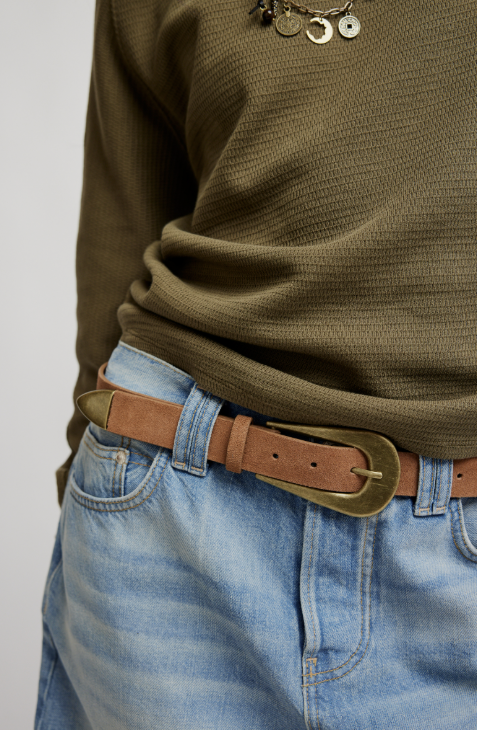 Person wearing a green sweater and blue jeans with a brown belt and gold buckle.
