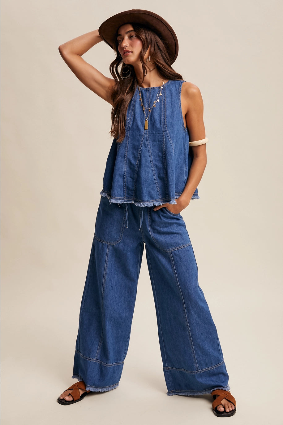 Woman wearing a denim outfit with wide-leg pants and a sleeveless top on a beige background