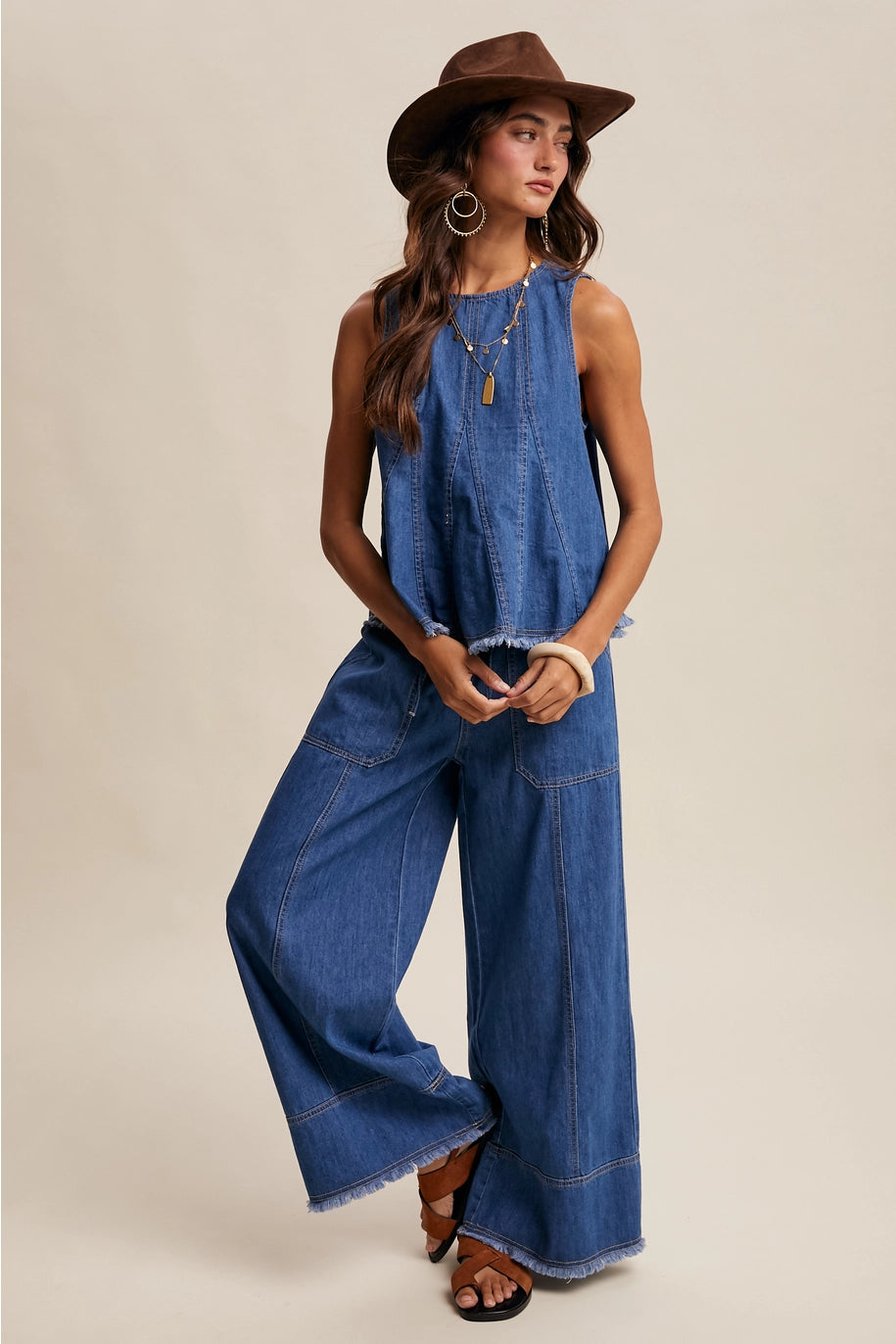 Woman wearing a blue denim jumpsuit with a brown hat on a beige background