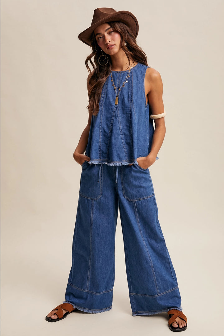 Woman wearing a blue denim jumpsuit with a brown hat on a beige background
