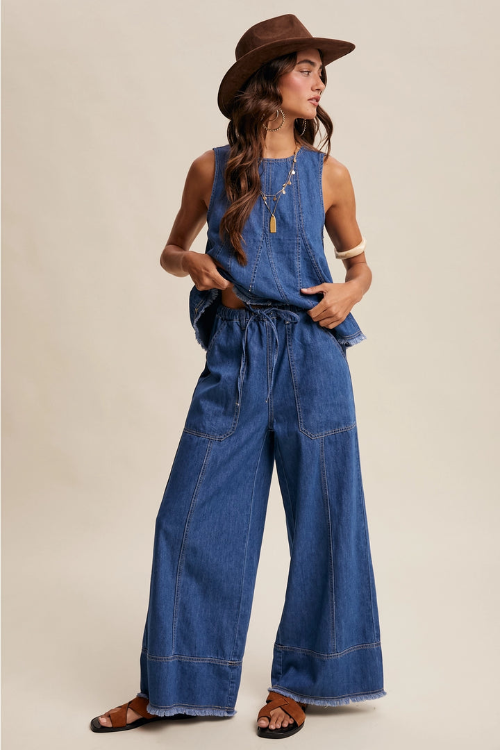 Woman wearing a blue denim jumpsuit and brown hat on a beige background